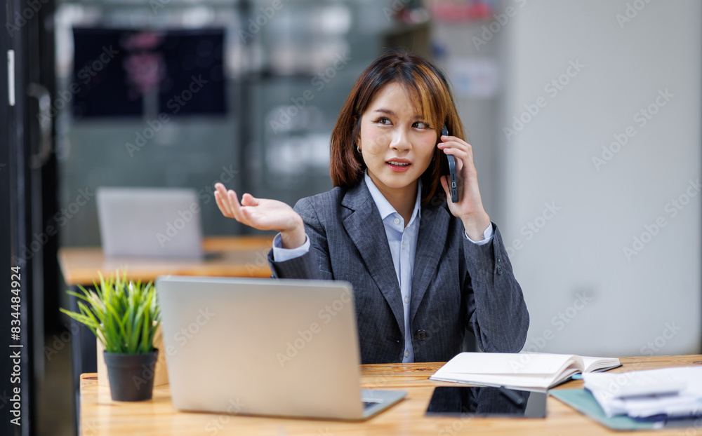 Asian woman entrepreneur busy with her work in the office. Young Asian woman work on desk laptop phone while planning sales, research or financial strategy in company

