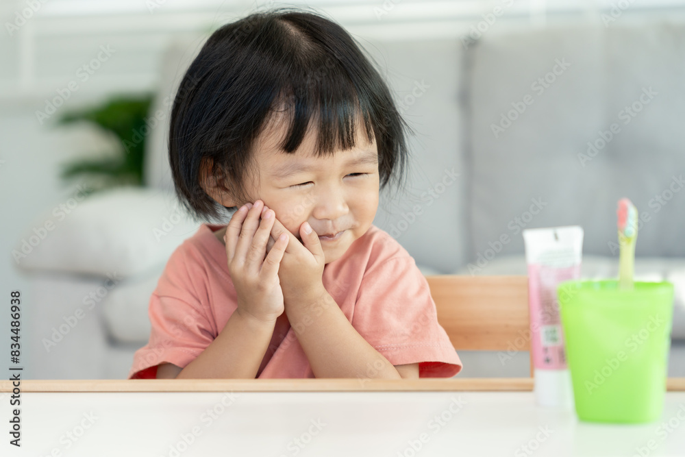 little asian girl presses hand to cheek, suffers from pain in tooth. Teeth decay, dental problems, child emotions and facial expression, oral health care, reducing sweets, fluorine coating little asian girl presses hand to cheek, suffers from pain in tooth. Teeth decay, dental problems, child emotions and facial expression, oral health care, reducing sweets, fluorine coating