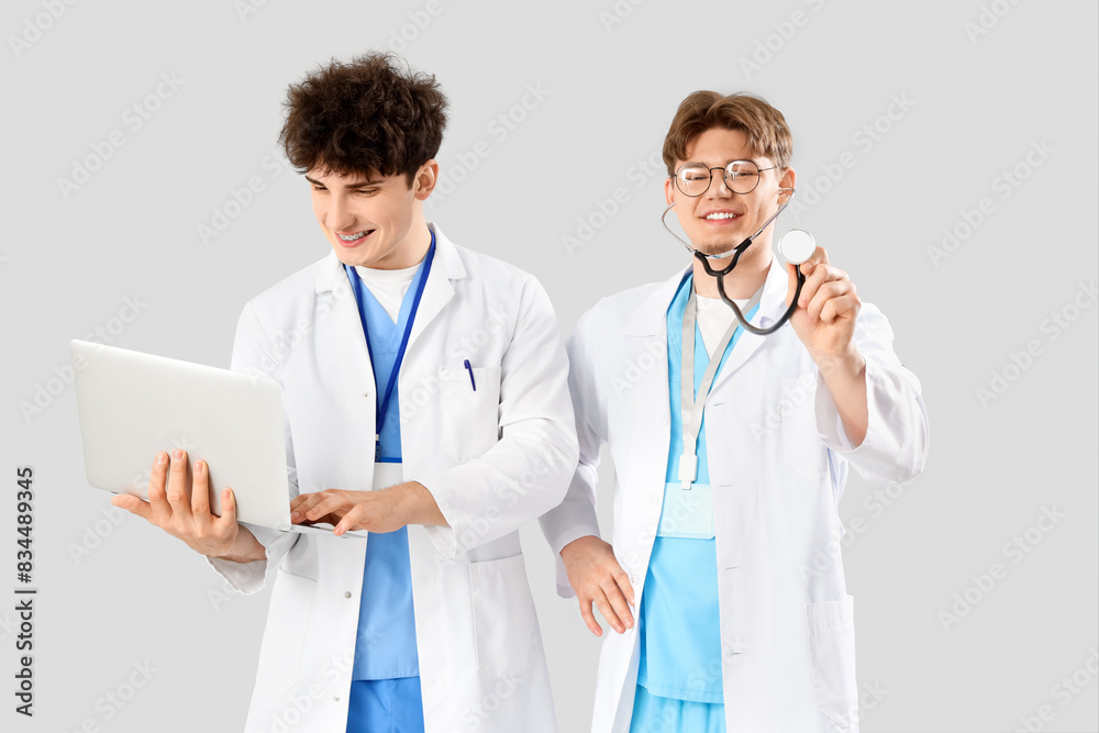 Male medical interns with laptop and stethoscope on light background Male medical interns with laptop and stethoscope on light background