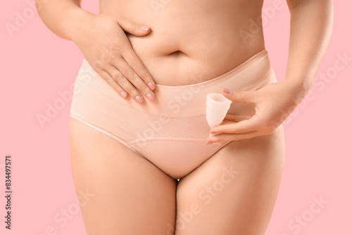 Young woman in period panties holding menstrual cup on pink background © Pixel-Shot