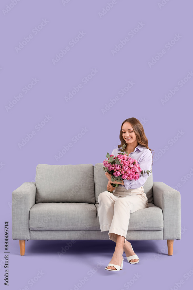 Beautiful young woman with roses sitting on sofa against lilac background Beautiful young woman with roses sitting on sofa against lilac background