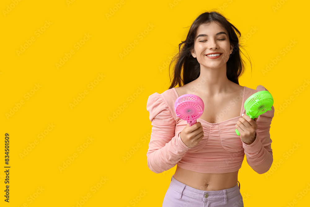 Young woman with mini fans on yellow background Young woman with mini fans on yellow background