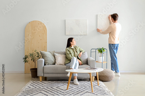 Young man hanging painting ...