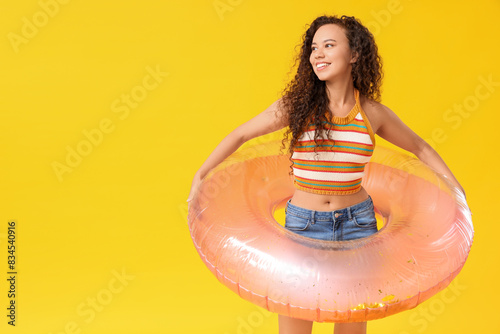 Beautiful young African-American woman with inflatable ring on yellow background © Pixel-Shot