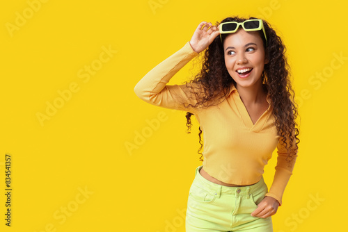 Beautiful African-American woman with sunglasses on yellow background