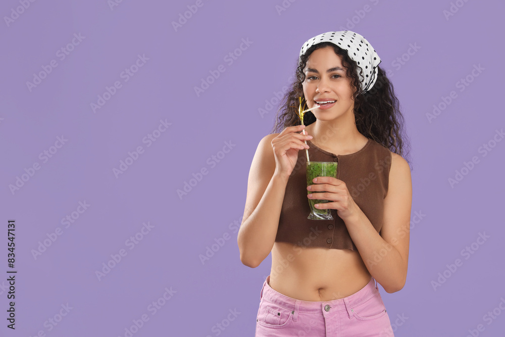 Fototapeta premium Beautiful young happy African-American woman with glass of tasty kiwi smoothie on purple background