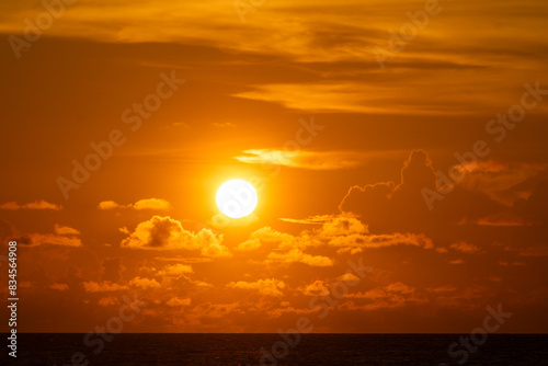 Big sun setting in Ocean painting orange the sky and the clouds