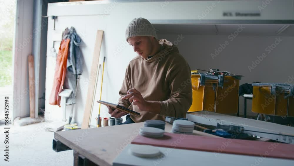 Young male worker sitting in concrete workshop creating design on digital tablet with stylus - shot in slow motion Young male worker sitting in concrete workshop creating design on digital tablet with stylus - shot in slow motion
