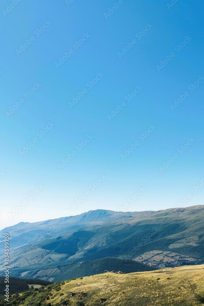 A serene mountain landscape with clear blue skies and rolling hills, offering a large area of copy space in the sky.