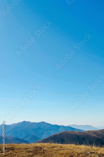 A serene mountain landscape with clear blue skies and rolling hills  offering a large area of copy space in the sky.