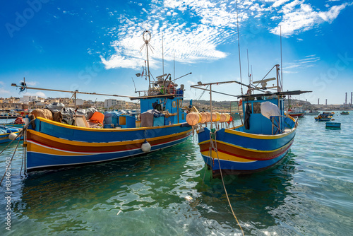 Traditional eyed colorful boats Maltese Luzzu in the turquoise blue water in the Harbor of Mediterranean fishing village Marsaxlokk, Cultural heritage of Malta.