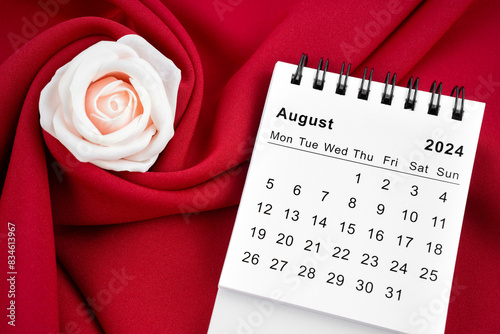 August 2024 desk calendar and pink rose on red textile. © gamjai