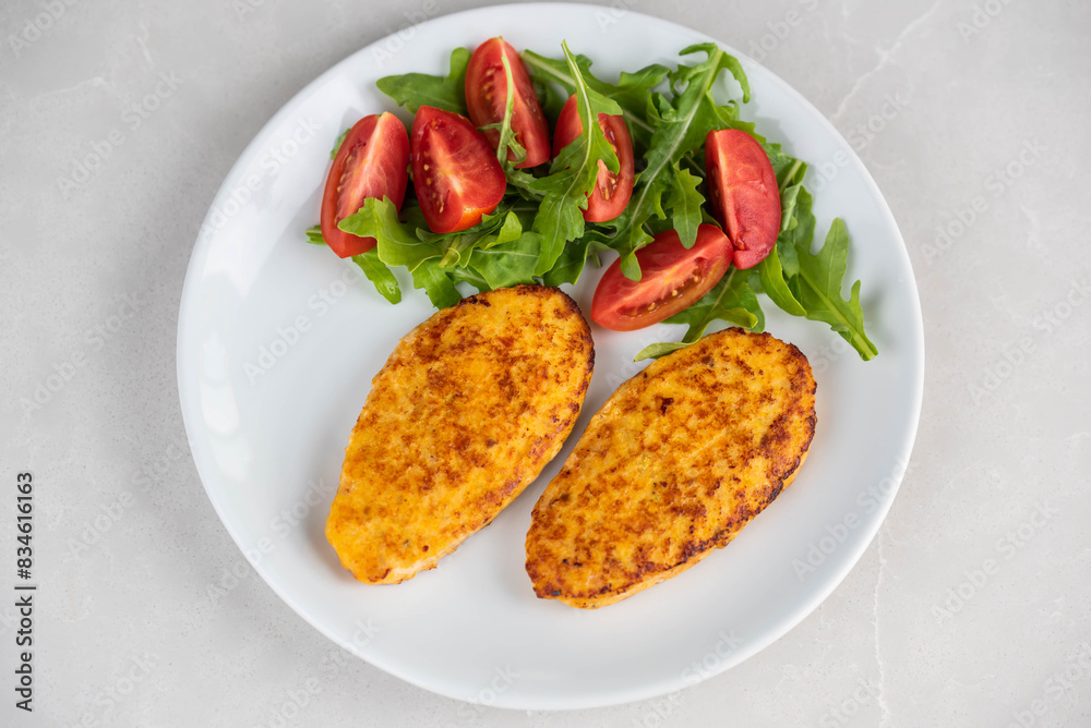 Fish cutlets being placed on a plate and garnished with arugula salad and cherry tomatoes. Concept of home cooking, traditional healthy food recipes, and culinary presentation. Fish cutlets being placed on a plate and garnished with arugula salad and cherry tomatoes. Concept of home cooking, traditional healthy food recipes, and culinary presentation.