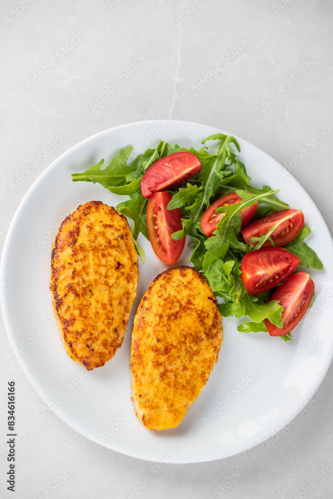 Fish cutlets being placed on a plate and garnished with arugula salad and cherry tomatoes. Concept of home cooking, traditional healthy food recipes, and culinary presentation. Fish cutlets being placed on a plate and garnished with arugula salad and cherry tomatoes. Concept of home cooking, traditional healthy food recipes, and culinary presentation.