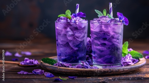  Two glasses of purpled iced tea  adorned with purple flowers and green leaves atop rims Presented on a wooden tray against a wooden surface  sprinkled with pur