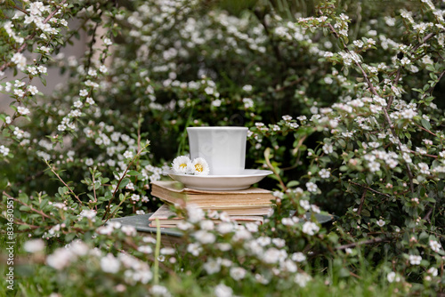 Coffee break with a cup of coffee among white flowers. Reading a book, concept of rest and leisure. Aesthetic lifestyle.