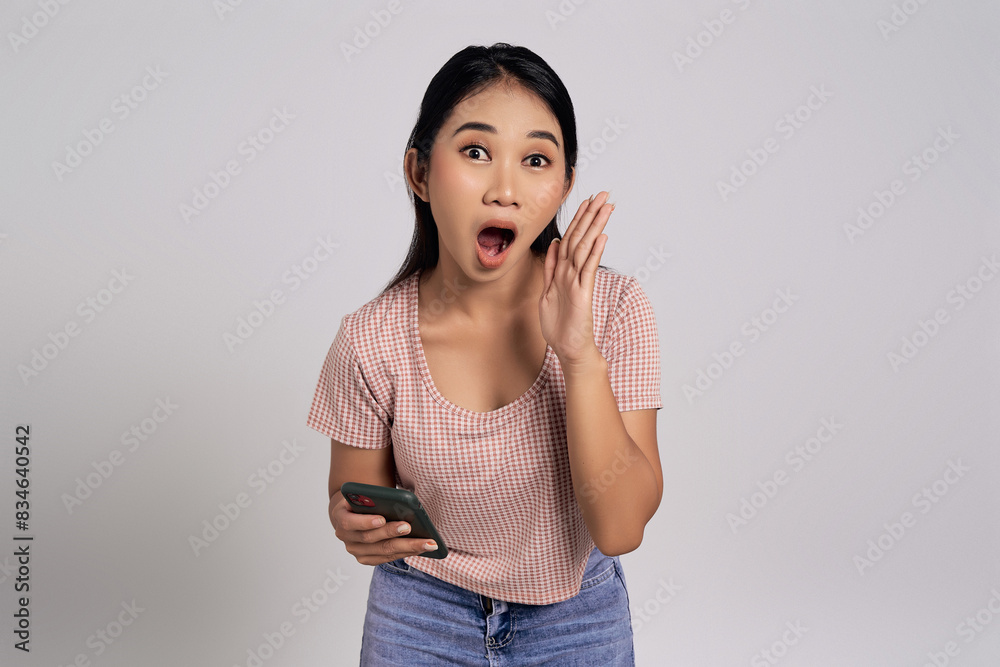 Excited beautiful young Asian woman in a casual t-shirt holding mobile cell phone and screaming on camera, announces offering a discount isolated on white background Excited beautiful young Asian woman in a casual t-shirt holding mobile cell phone and screaming on camera, announces offering a discount isolated on white background