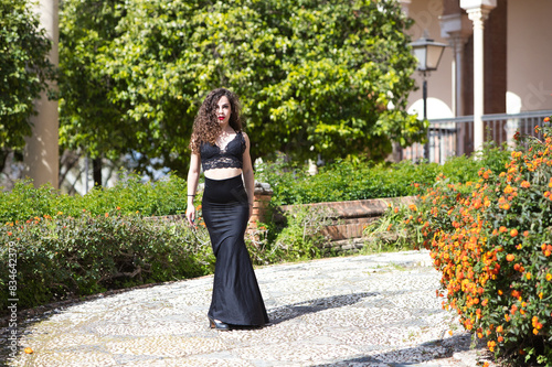 Beautiful woman with long curly hair, walks in a park in Seville, Spain. Dressed in long black skirt and black top. The woman is a flamenco dancer and takes advantage of her break to visit the city.