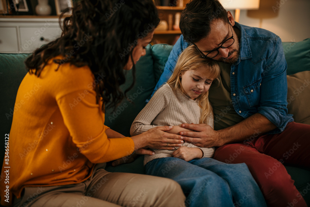 Naklejka premium Worried father and mother consoling their little girl who is having stomachache at home