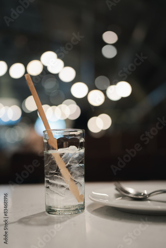 Glass of water with ice cube on cafe bokeh blurred background