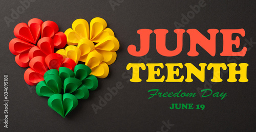 From top view, a collection of small paper hearts arranged into a large heart shape in Juneteenth's symbolic colors - red, green, yellow against a black background, offering space for social text photo