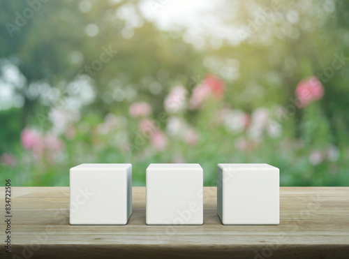 Three white block cubes on wooden table over blur pink flower and tree in garden