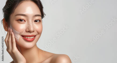 Portrait of beautiful young asian woman with clean fresh skin on white background, happy smile and hand touch face isolated over grey color backdrop. Beauty treatment concept.