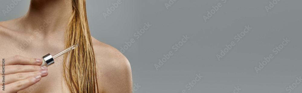 Obraz premium Alluring woman holding a hair serum, displaying her hair care routine with wet hair.
