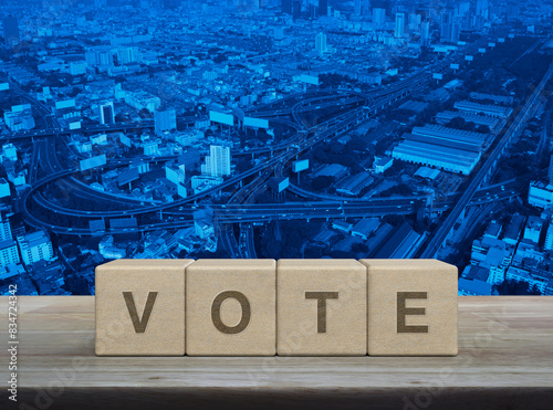 Vote letter on wood block cubes on wooden table over modern city tower, street, expressway and skyscraper, Election and voting concept