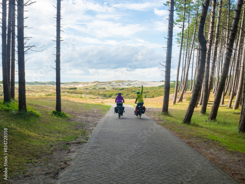 Egmond, Netherlands - August 5th 2023: Two cyclists leaving a forest towards sand dunes on North Sea Cycling Route.