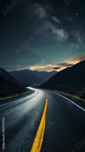 Empty highway along a mountainous area under a dark sky at sunset.