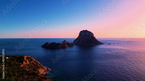 Aerial view of sun setting behind Es Vedra Ibiza during sunset. Showing ocean and clear skies.