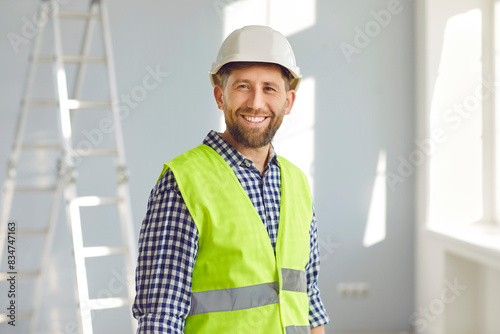 Happy smiling male builder repairman in safety helmet and reflective jacket. Portrait of positive handsome foreman looking at camera. Builder profession, construction concept