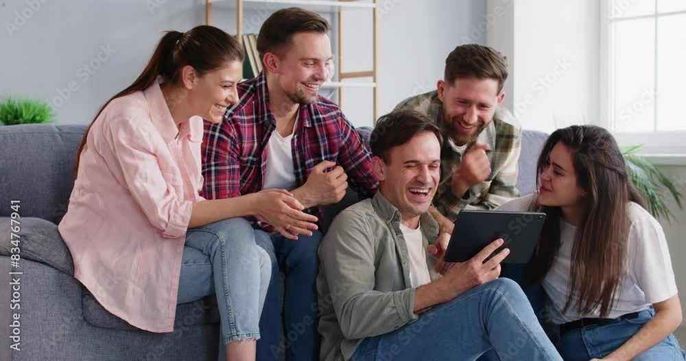 Positive friends sitting on a sofa during a home party, using a tablet for online entertainment, spending leisure. Talking and laughing, enjoying each other company, internet and people togetherness. Positive friends sitting on a sofa during a home party, using a tablet for online entertainment, spending leisure. Talking and laughing, enjoying each other company, internet and people togetherness.