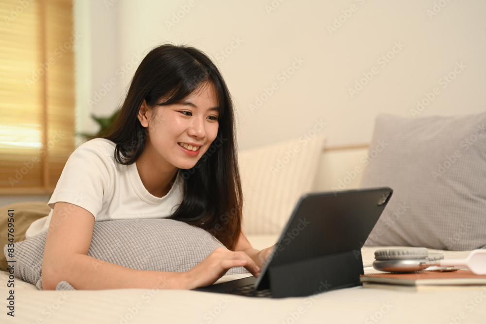 An attractive young Asian woman using digital tablet while lying on her bed An attractive young Asian woman using digital tablet while lying on her bed