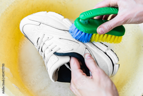 Cleaning white sneakers with a brush and detergent in a basin. © Natallia