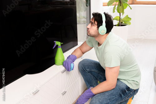 Young man in headphones wiping television with a rag and spray