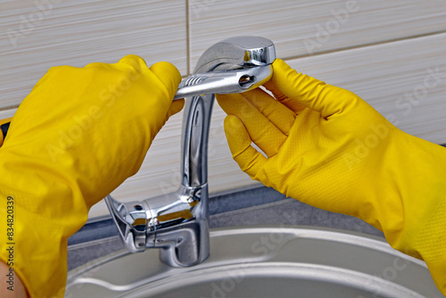 Kitchen faucet repair. A worker in yellow rubber gloves uses an adjustable wrench to unscrew the aerator