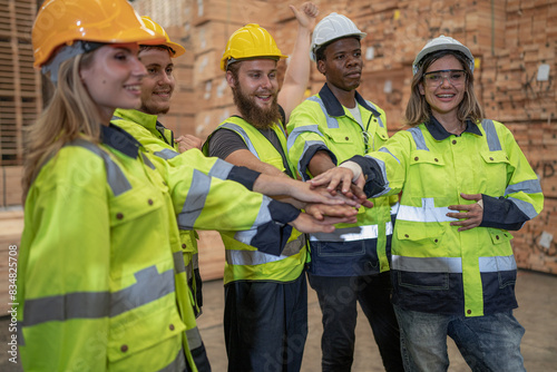 Group of diverse people wear safety helmet and vest uniform standing in factory. Young women engineer and men colleague in hard hat working together, portrait. Manufacturing teamwork. Selective focus