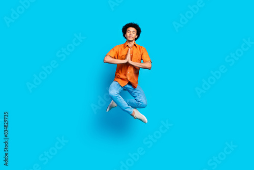 Full length photo of handsome good mood guy wear orange shirt jumping high praying isolated blue color background © deagreez