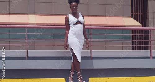 On a city rooftop, a black girl in a white dress stands overlooking the skyline. photo