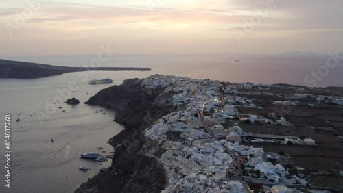 DRONE SHOT OF SANTORINI GREECE CLIFFSIDE AND WHITE HOUSES AT SUNSET BOATS MARINA 4K photo