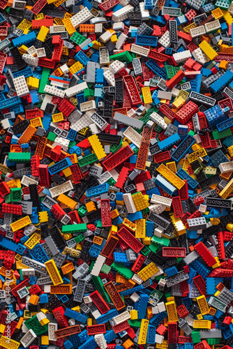 A chaotic yet colorful jumble of toy bricks, tightly packed to fill the entire frame. The bricks come in various sizes and an array of colors including red, blue, green, yellow, and white, © grey