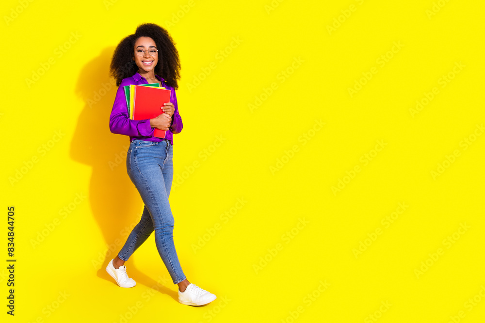 Full body photo of attractive young woman hold books walking dressed stylish violet clothes isolated on yellow color background Full body photo of attractive young woman hold books walking dressed stylish violet clothes isolated on yellow color background