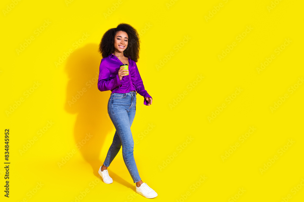 Full body photo of attractive young woman hold paper cup walking dressed stylish violet clothes isolated on yellow color background