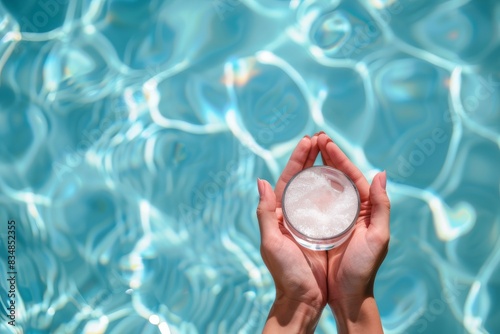 female hands holding a jar of cream against the background of blue pool water, mock up, spf, moisturizing cream for the summer