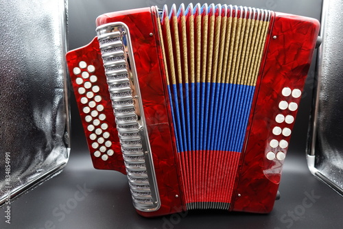 A vibrant red Colombian vallenato accordion featuring the colors of the Colombian flag (red, yellow, and blue). This traditional musical instrument is commonly used in Colombian folk music and is char