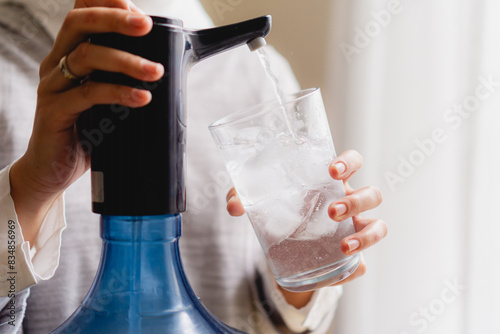 pumping water from gallon using electric water pump in glass filled with ice cubes