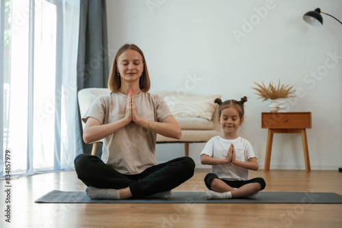 Calm, in lotus pose. Young woman with little girl are doing yoga at home