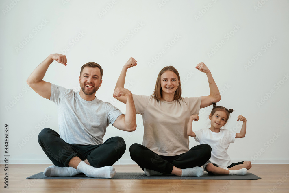 Showing the biceps, strong. Family of mother, father and daughter are doing yoga at home Showing the biceps, strong. Family of mother, father and daughter are doing yoga at home